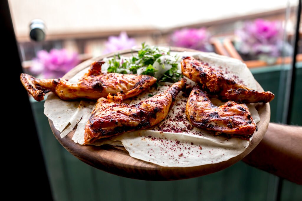 front view a man holds a tray with grilled chicken thighs on a pita with onions and herbs
